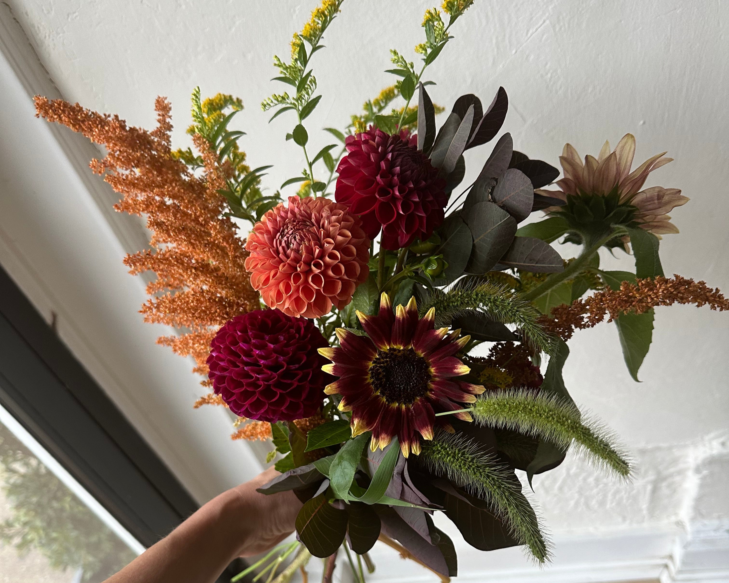 Bouquet of flowers being held against a window with a wooden frame.