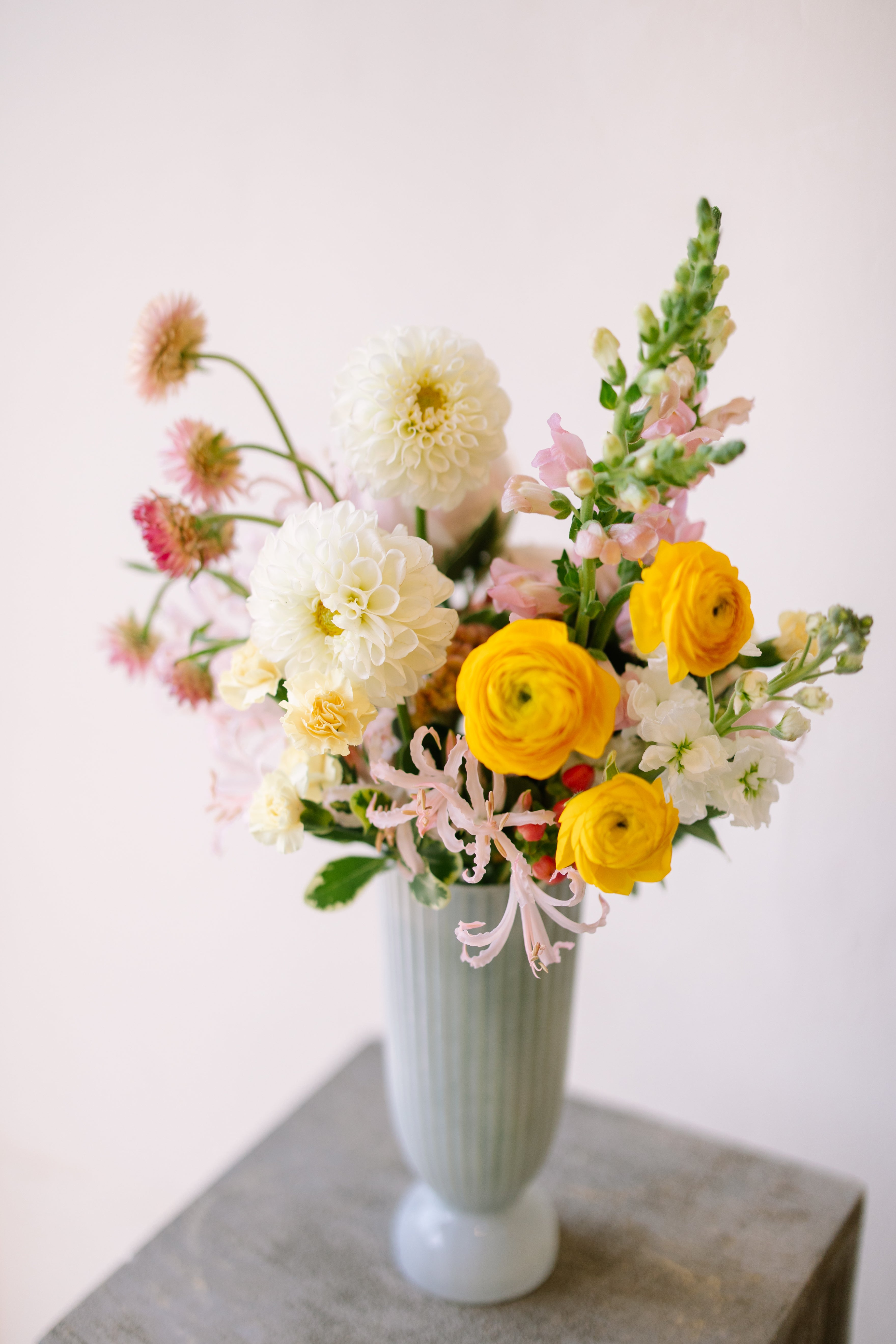 Tall garden flower arrangement in white footed vase.