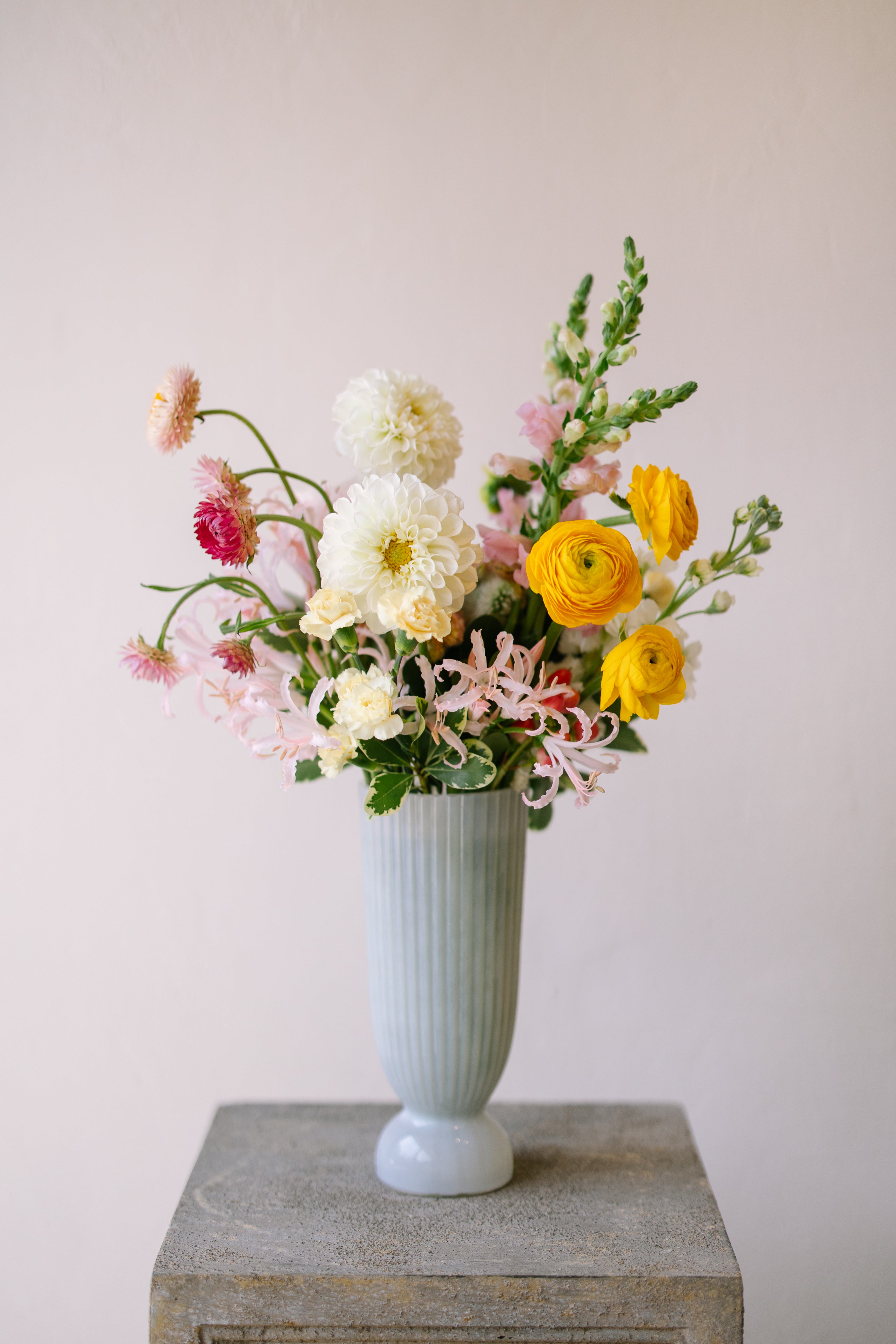 Tall garden flower arrangement in white footed vase.