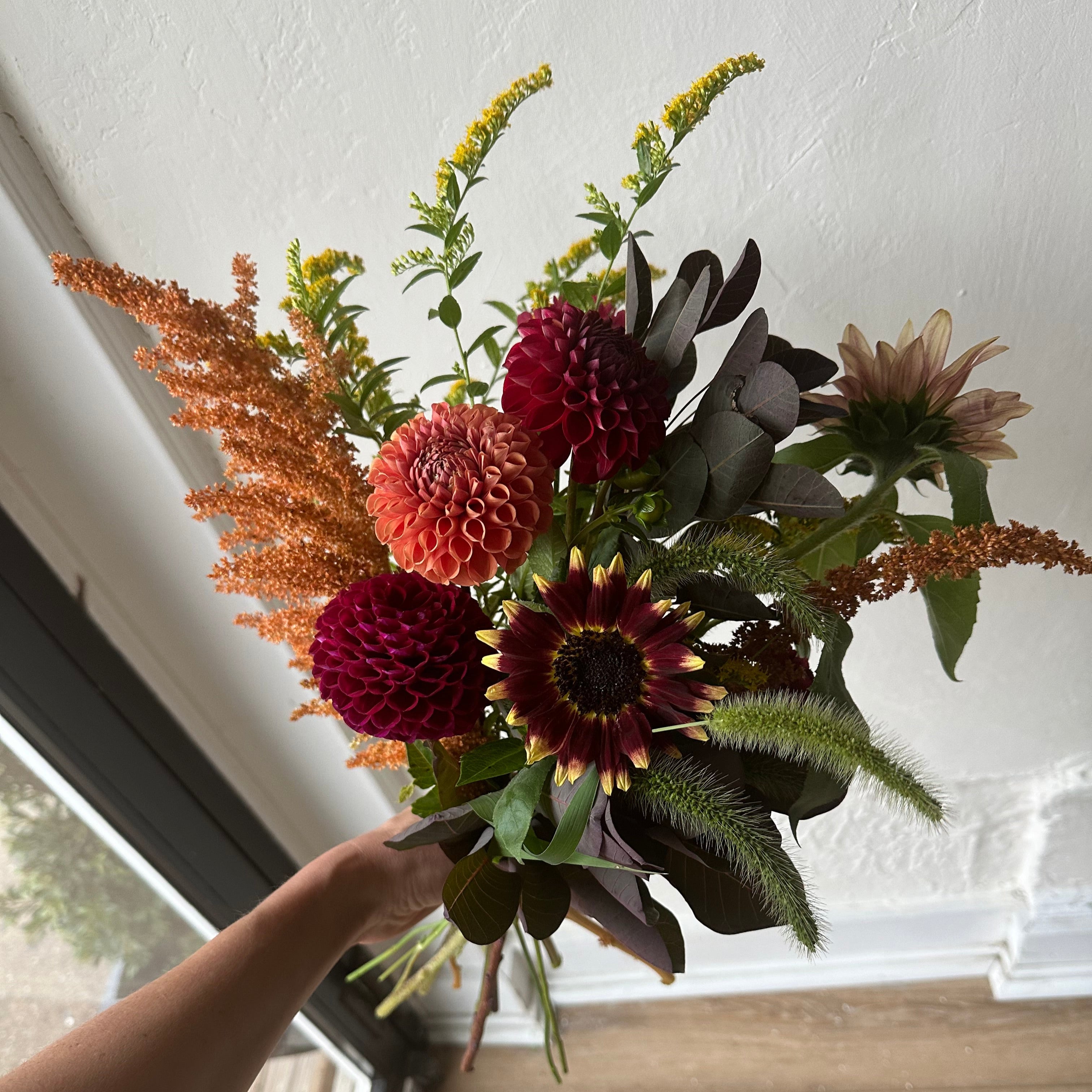 Bouquet of flowers being held against a window with a wooden frame.
